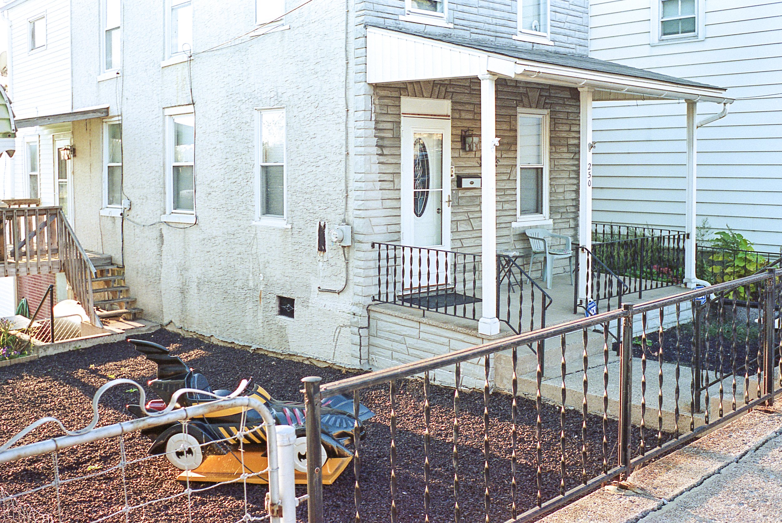 Backyard with small porch, children’s toys, and fencing next to two-story houses with light-colored siding.