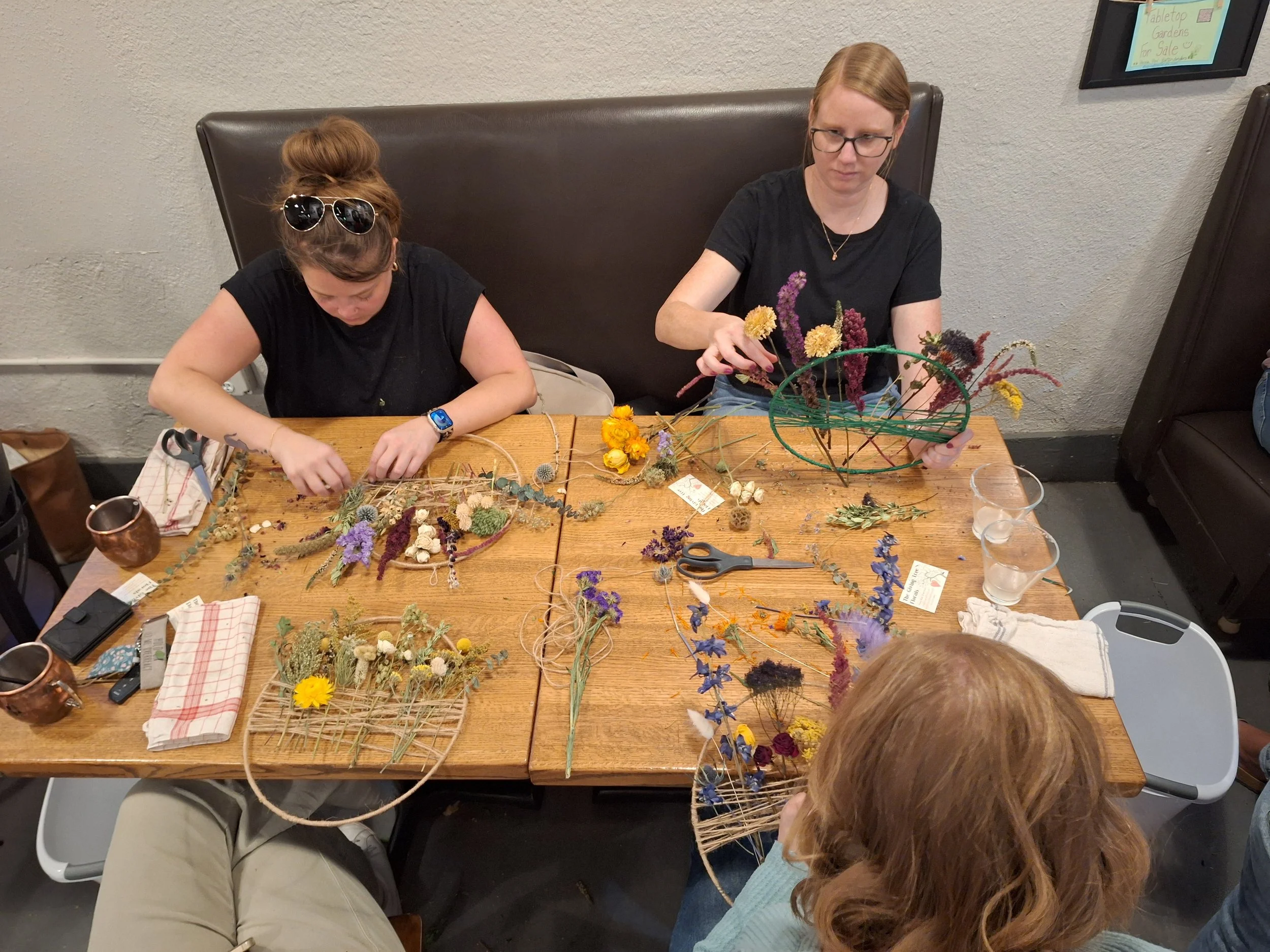 People at a table creating floral arrangements with dried flowers, scissors, and floral wires.