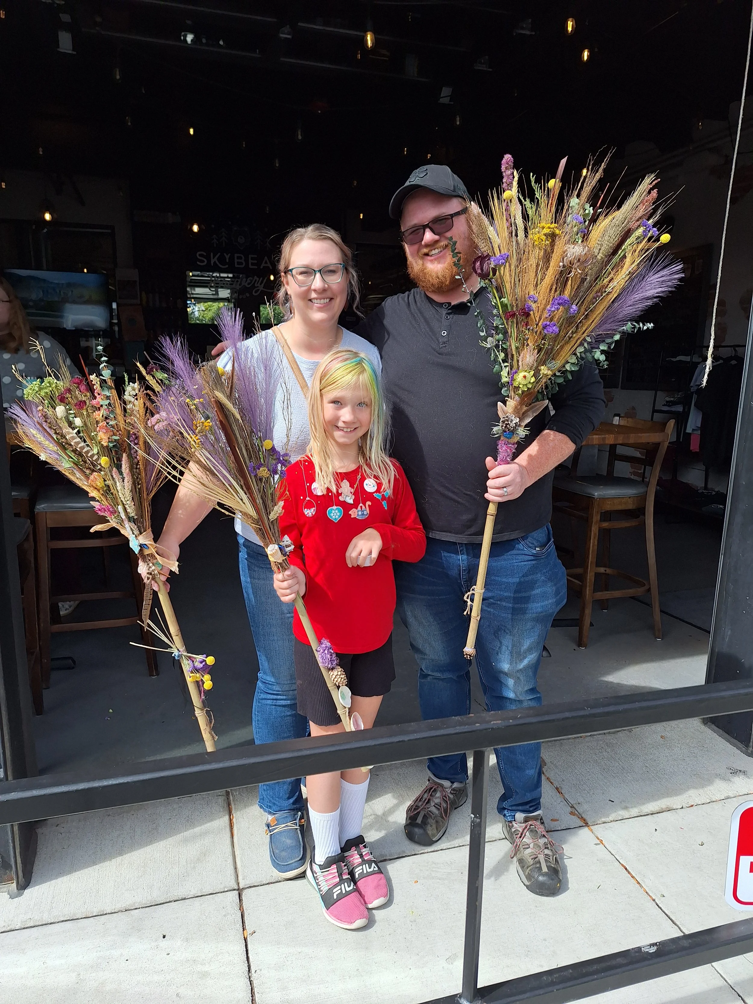 A family of three posing with bouquets of dried flowers outside a shop.