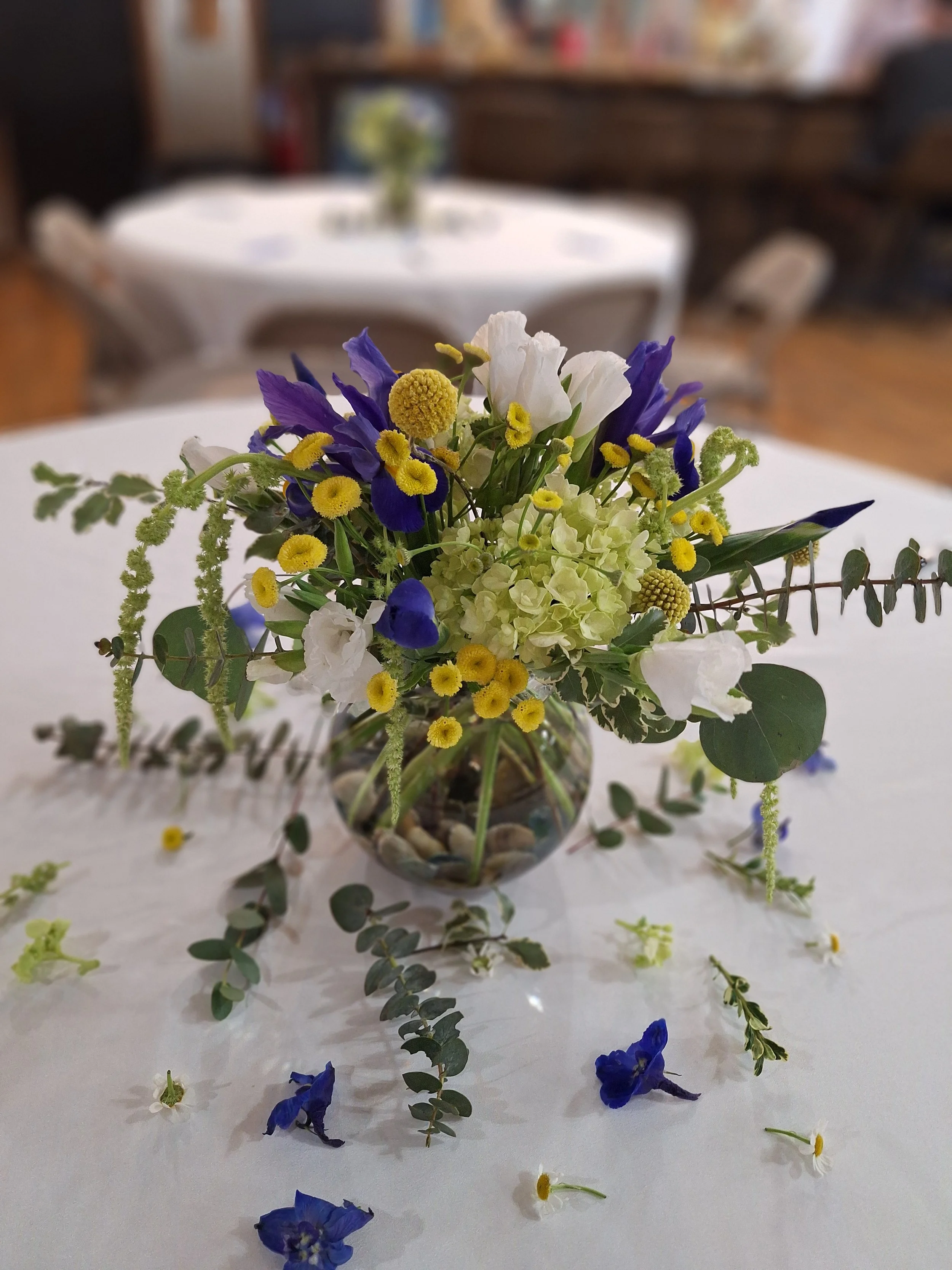 Group of ten women and one young girl holding floral arrangements in an indoor setting with a large photo of a bear on the wall behind them.