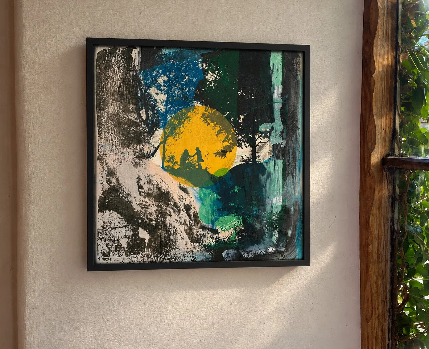 Framed abstract painting with a yellow circle, layered blue, green, black, and white brushstrokes on a textured wall