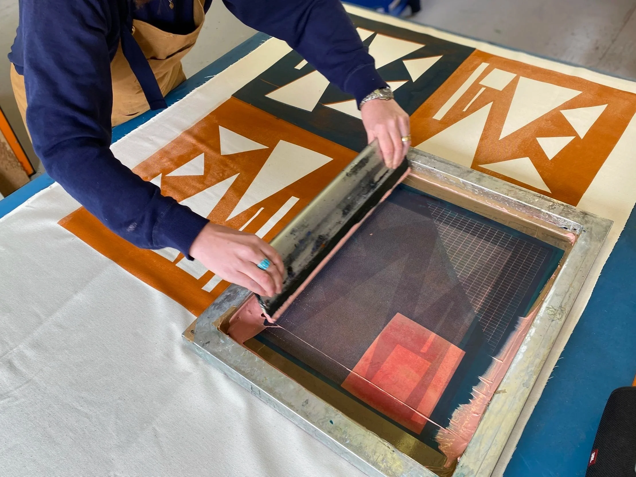 Person screen-printing an abstract geometric design onto fabric using a squeegee and screen-printing frame