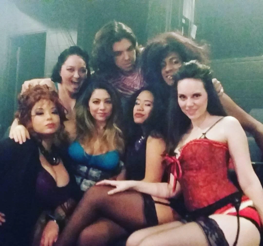 ROCK OF AGES a rock musical at Manoa Valley Theatre. Group of women with large hair and colorful clothing, posing closely together in a dimly lit room.