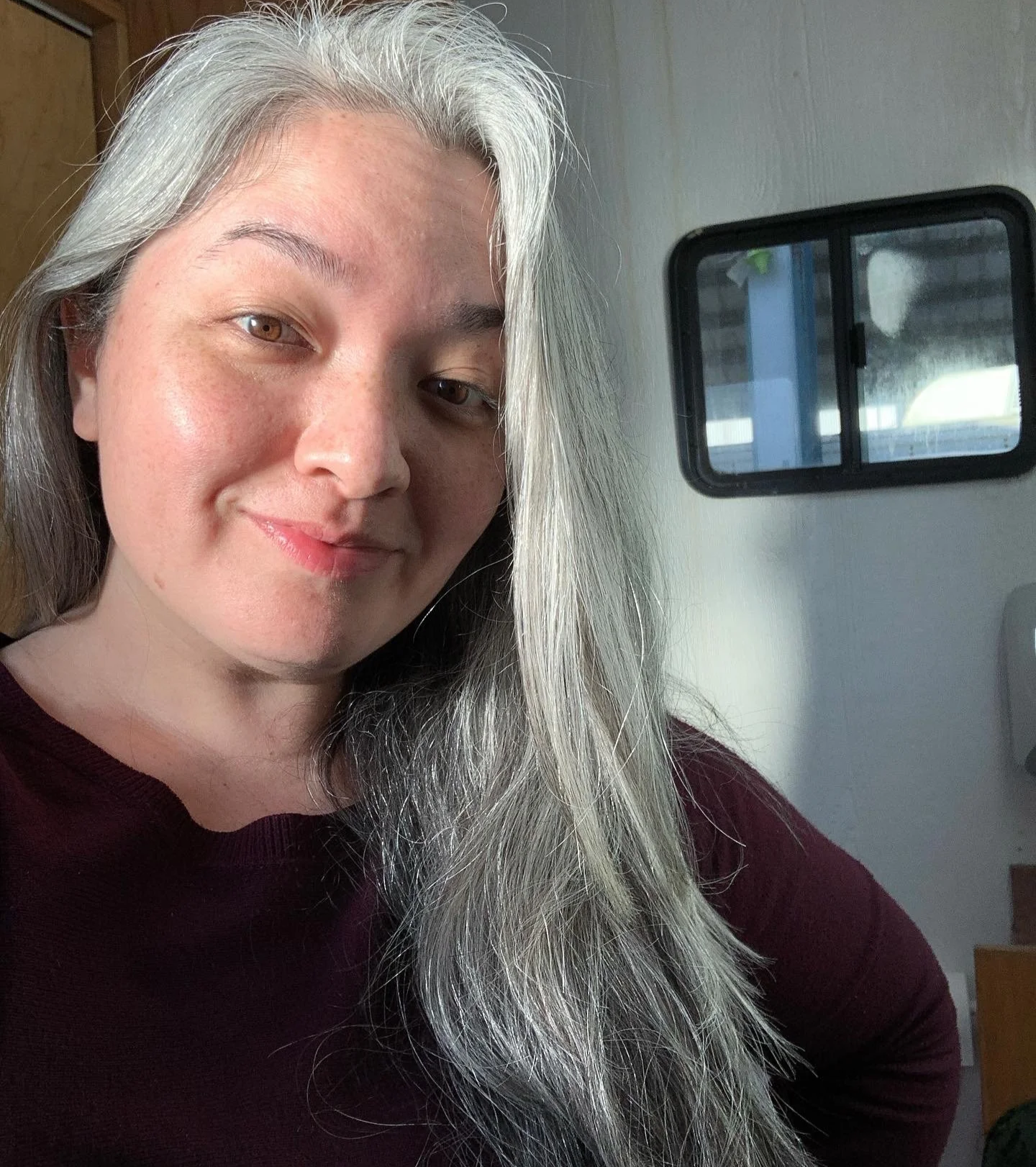 On set filming for MAGNUM P.I. with CBS on the studio lot in Honolulu, Hawaii. A SAG-AFTRA actress with long silver hair and a slight smile, sitting inside a movie trailer.