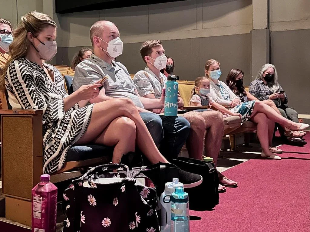 WAITRESS the Broadway musical by Sara Bareilles at Diamond Head Theatre. Time for notes in the house. Group of actors sitting in theater seats, wearing masks, with bags and water bottles in front of them.