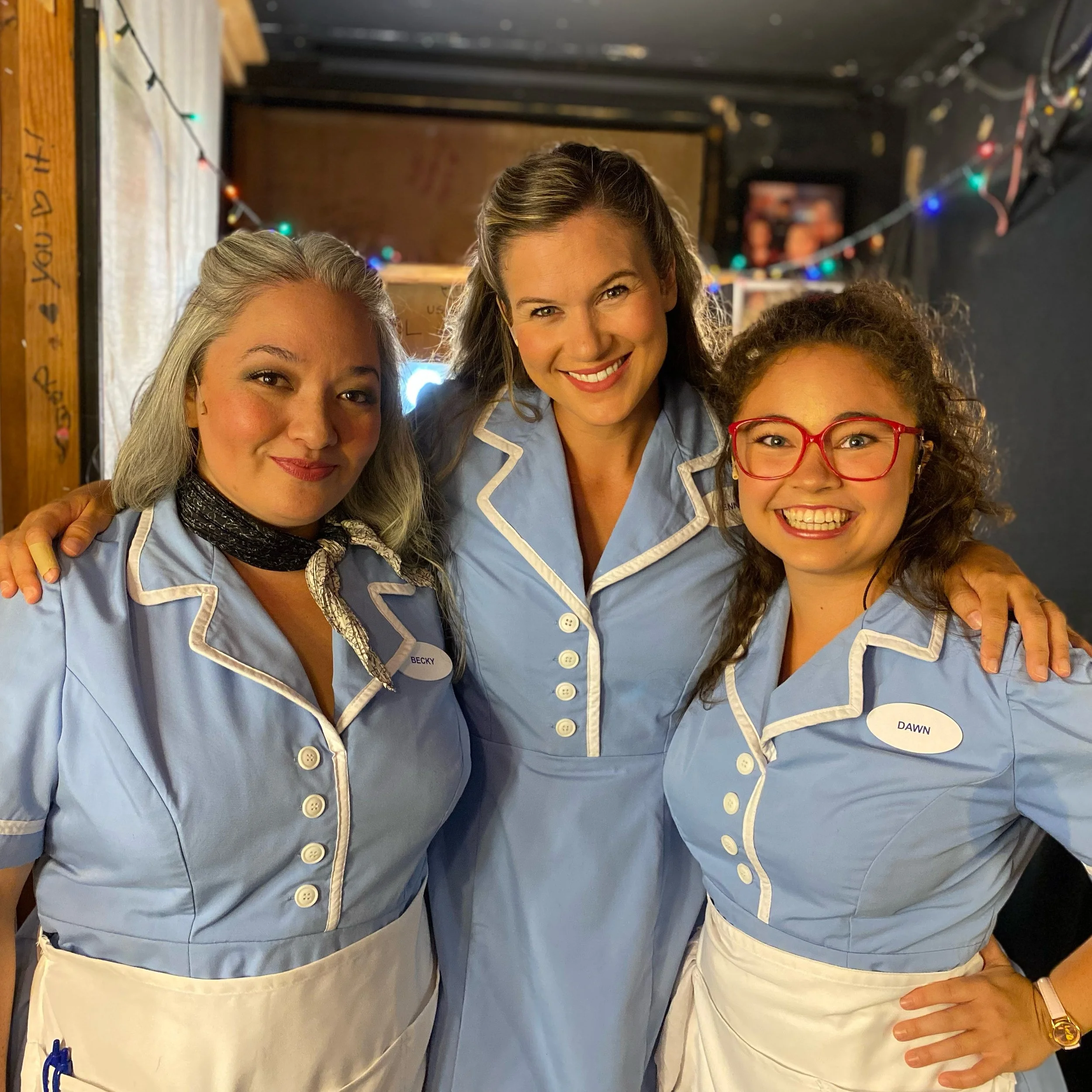 WAITRESS the Broadway musical at Diamond Head Theatre. The three waitresses in blue uniforms with white trim, backstage, posing together in the dressing room. Cassie Favreau-Chung (Becky), Sarah Souza (Jenna), and Karese Kaw-uh (Dawn).