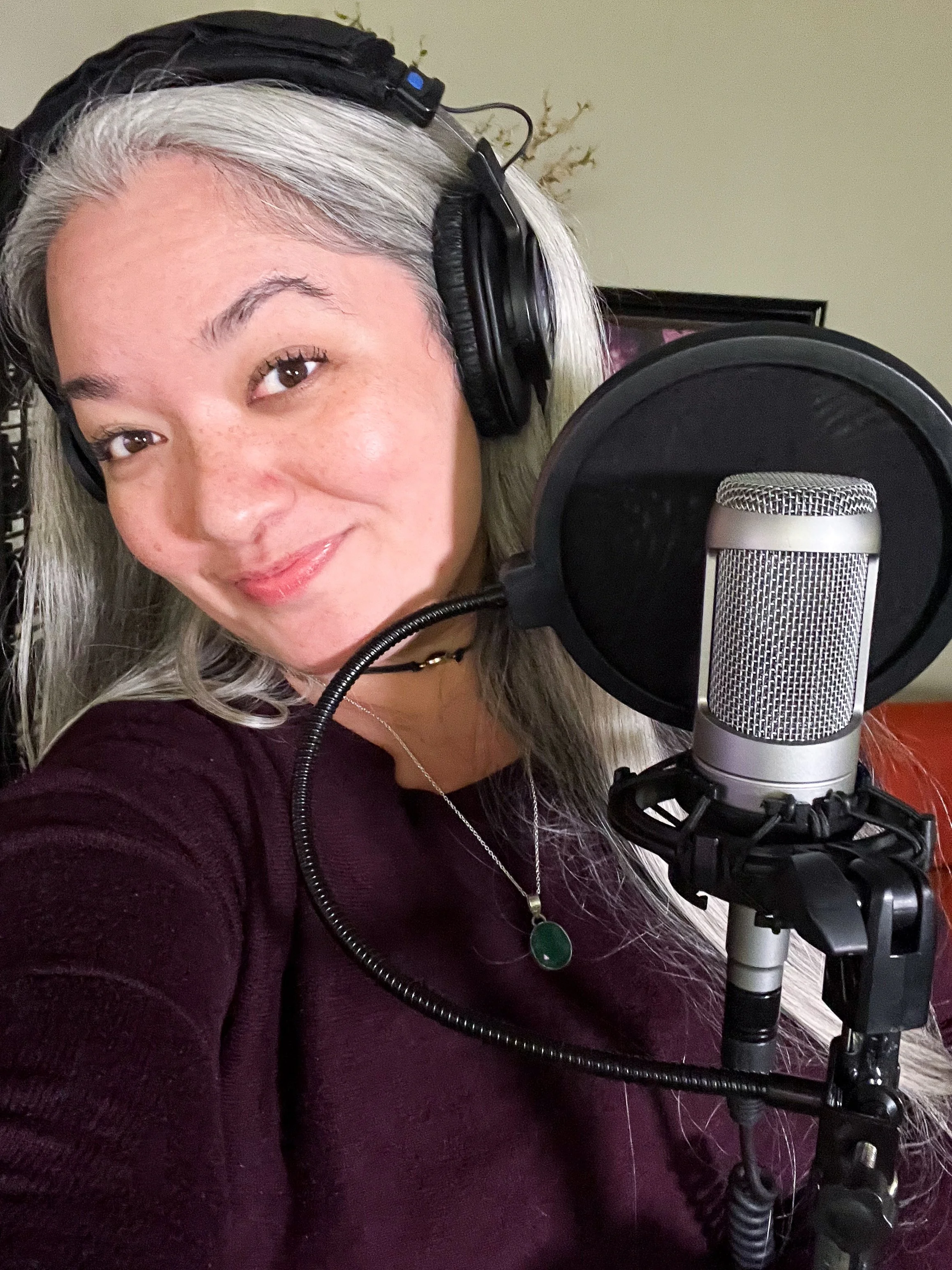 Hawaii SAG-AFTRA voiceover actor. Woman with gray hair wearing headphones, standing in front of a microphone in a recording studio.