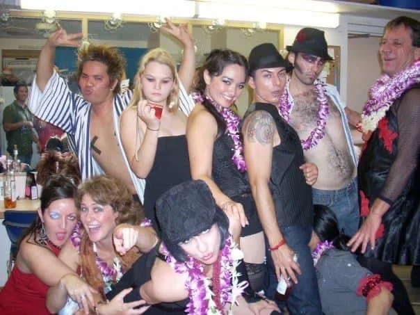 ROCKY HORROR SHOW AT Manoa Valley Theatre. Actress Cassie Favreau-Chung plays Magenta. Group of people dressed in party attire with leis, posing for the camera in a social setting.