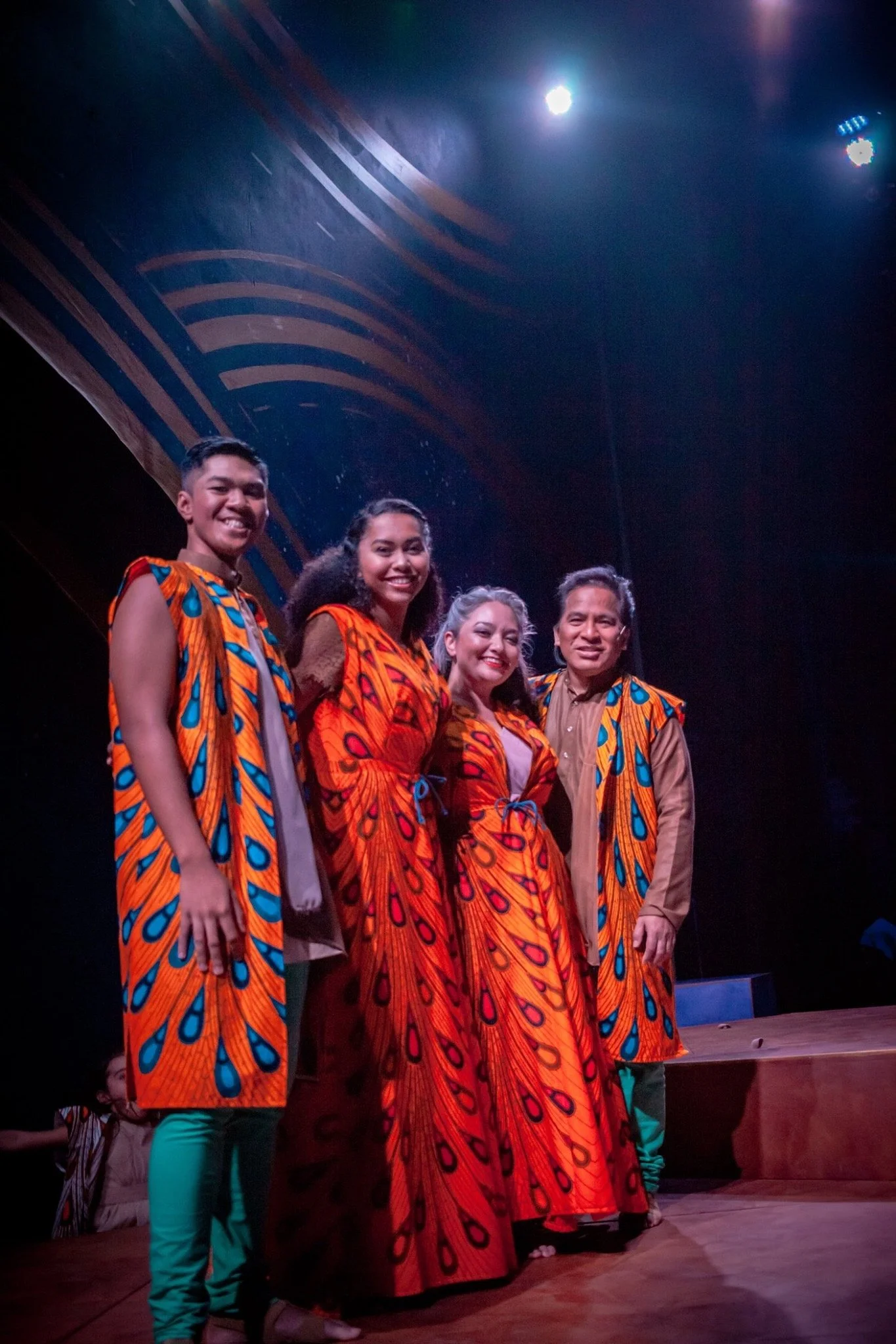 CHILDREN OF EDEN a Broadway musical by I'm A Bright Kid. Group of five people standing on stage, dressed in traditional African-style clothing with bright orange and blue patterns, smiling and posing for the photo at a cultural event or performance.