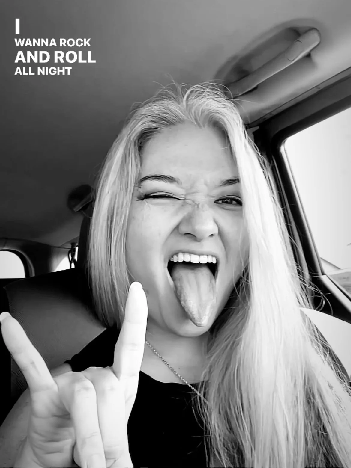 A young woman with long silver hair making a face with her tongue out and one eye closed, inside a vehicle. She is holding up her left hand in a rock and roll gesture. Text on the image reads: 'I WANNA ROCK AND ROLL ALL NIGHT.'