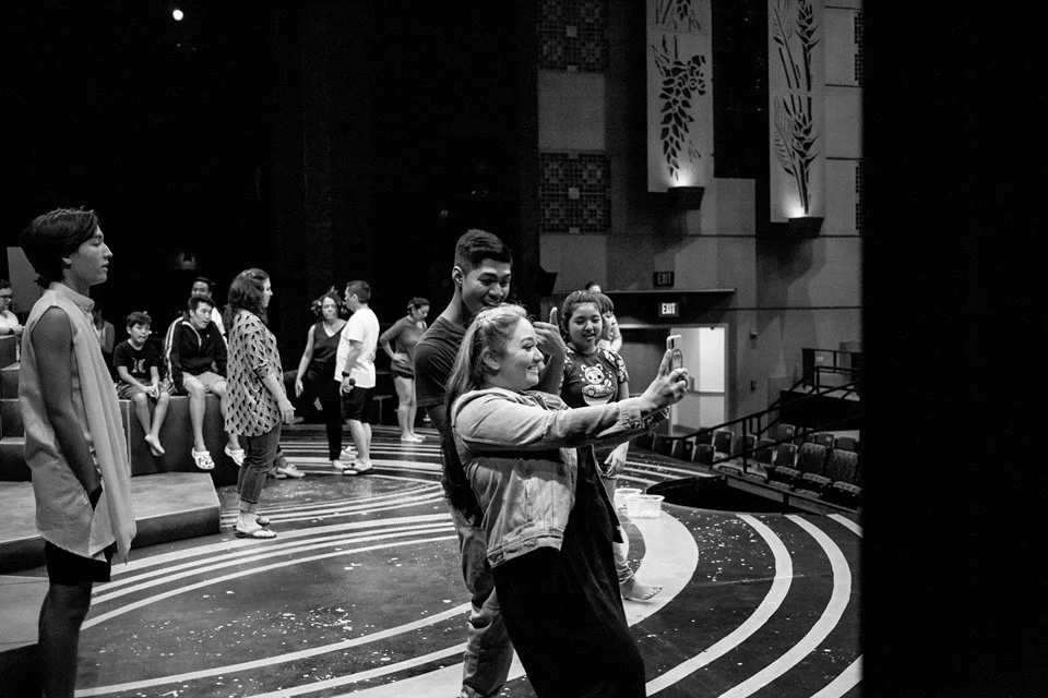CHILDREN OF EDEN a Broadway musical by I'm A Bright Kid Foundation at Paliku Theatre. Group of young people on stage in an auditorium, some taking selfies and others waiting or talking.