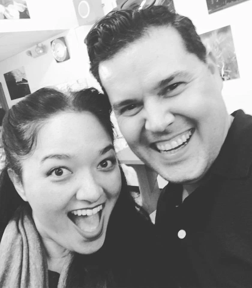 Actors Cassie Favreau-Chung and Kevin Pease. Next To Normal royalty. Hawaii actors. A black and white photo of a woman and man smiling and posing for a selfie, indoors with pictures hanging on the wall in the background.