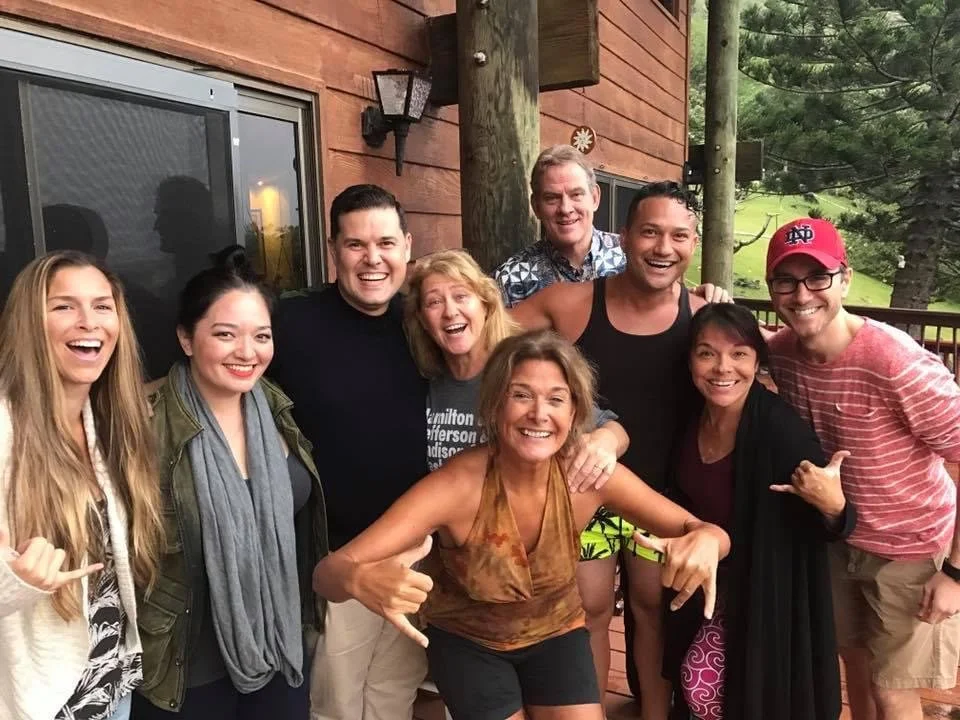 RISE UP: A BENEFIT CONCERT BY MELINA LILLIOS at Paliku Theatre in Kaneohe, Hawaii. Group of people smiling and posing together on a wooden porch outside a house with greenery in the background.