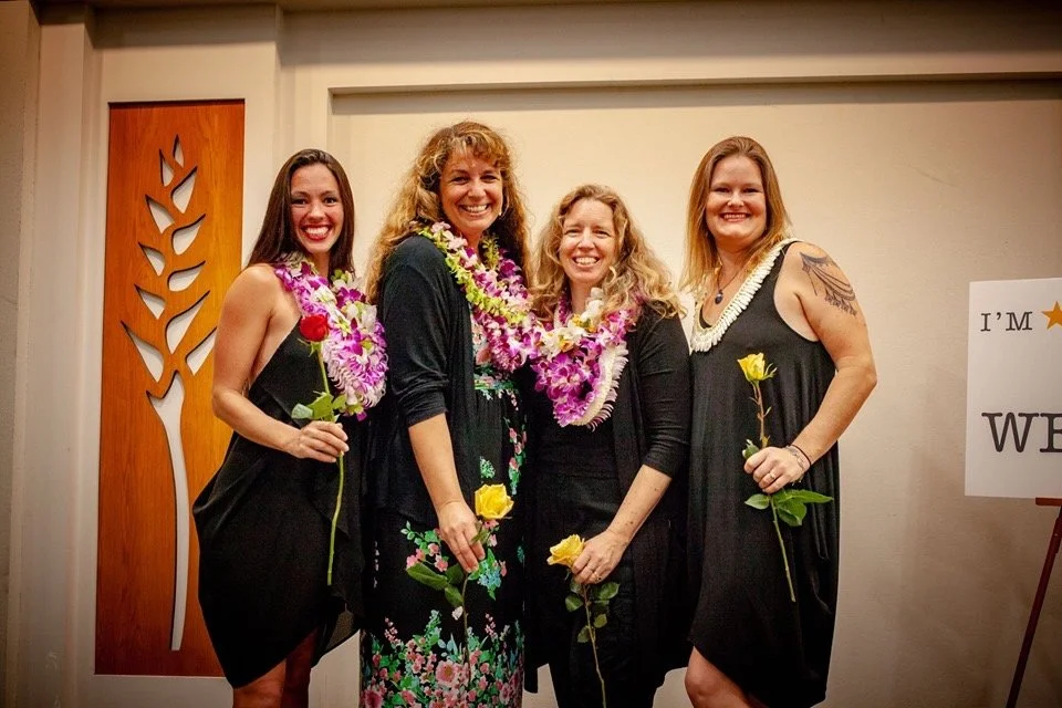 CHILDREN OF EDEN a Broadway musical by I'm A Bright Kid Foundation at Paliku Theatre. Four women standing together at a celebration, wearing leis, holding yellow roses, and smiling.