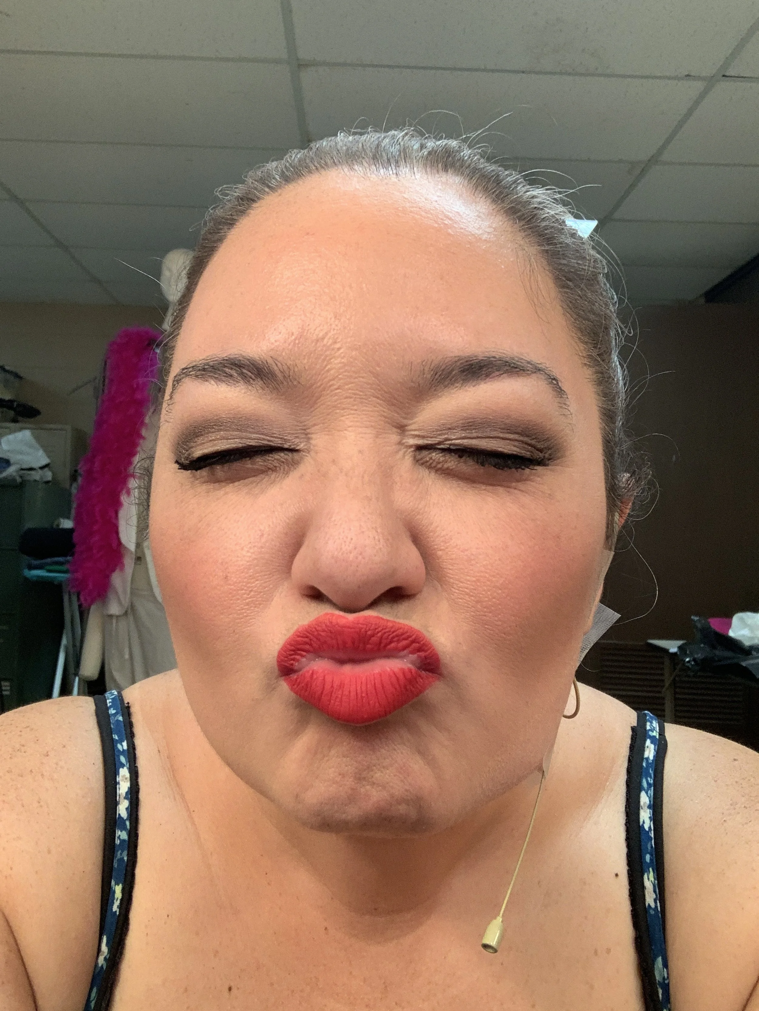 THE 25TH ANNUAL PUTNAM COUNTY SPELLING BEE a comedy musical at Manoa Valley Theatre in Honolulu, Hawaii. A woman with closed eyes and puckered lips, wearing red lipstick, makeup, and a sleeveless top, in an indoor setting. Actress