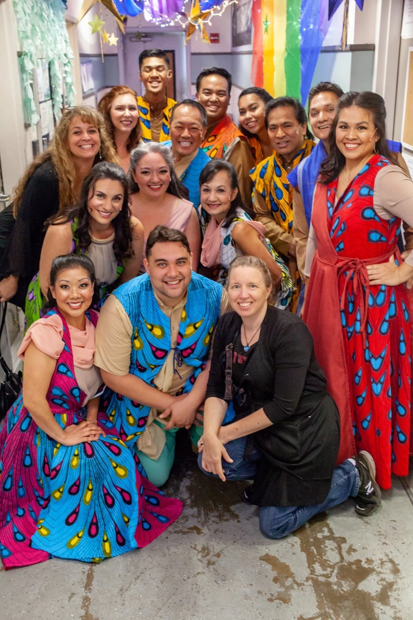 CHILDREN OF EDEN a Broadway musical by I'm A Bright Kid Foundation at Paliku Theatre. Group of people celebrating at a classroom decorated with rainbow banners and star paper decorations.