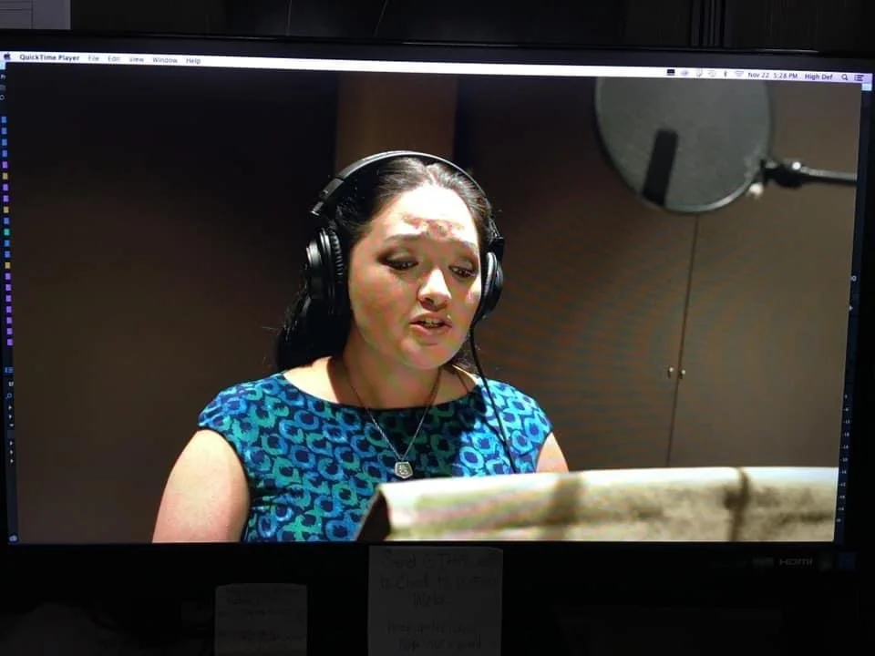 Hawaii voiceover actor. A woman in a recording studio at Blue Planet Sound at Hawaii News Now wearing headphones, singing or speaking into a microphone, with a music stand in front of her.