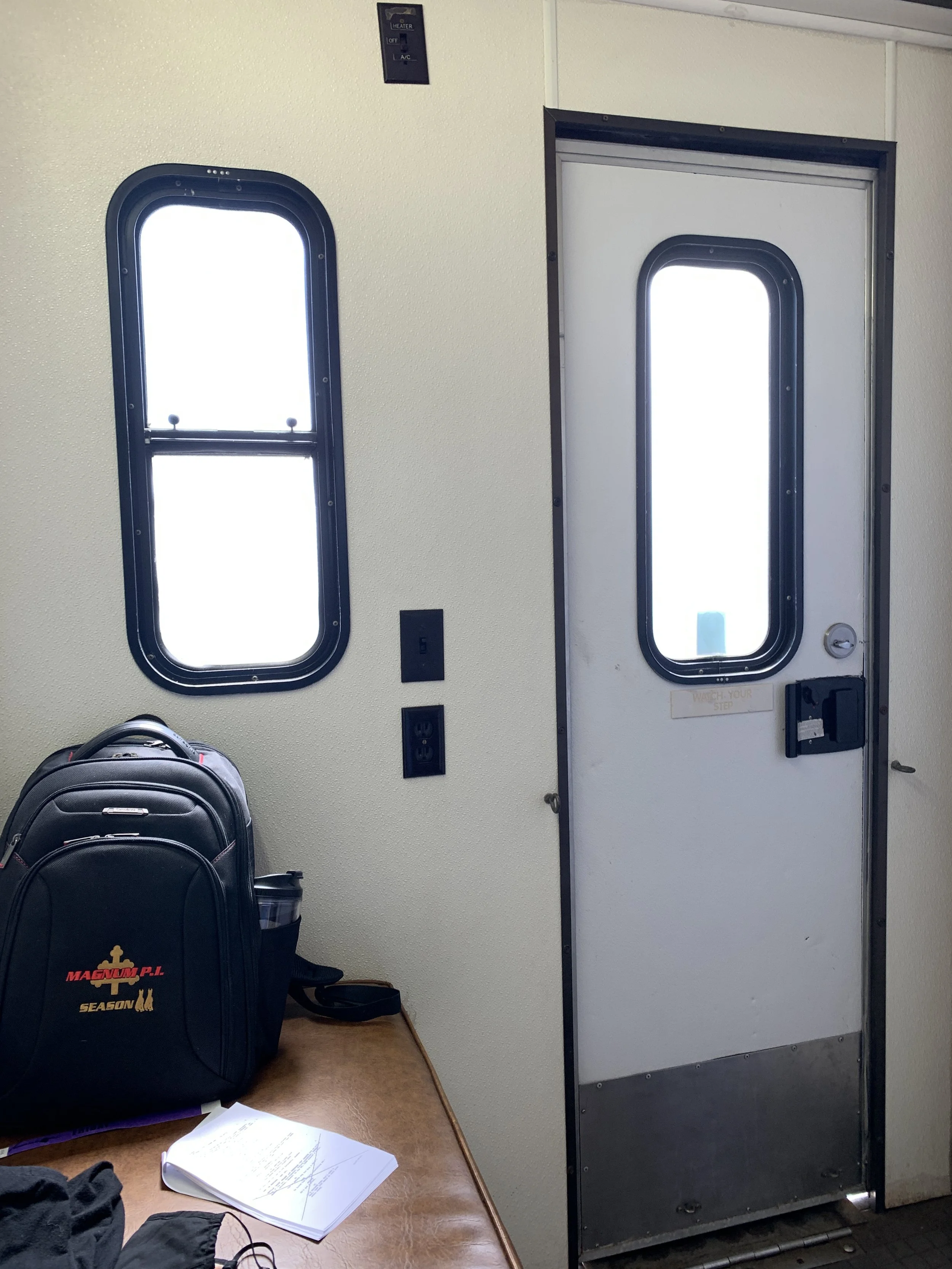 On set filming for MAGNUM P.I. with CBS on the studio lot. Interior of a train or bus with a door and window, a black backpack on a wooden table, and some papers.
