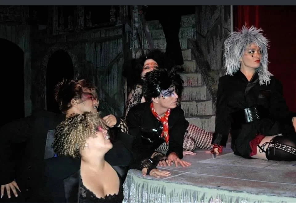 ROCKY HORROR SHOW AT Manoa Valley Theatre. Actress Cassie Favreau-Chung plays Magenta. The image shows a theatrical performance with five actors in costumes resembling punk or goth style, on stage with a dark, spooky background.
