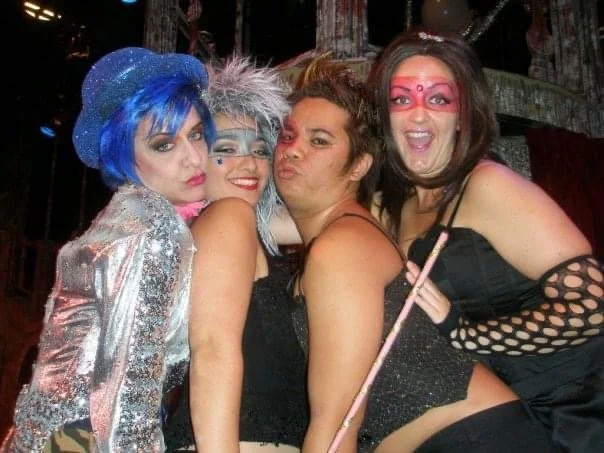 ROCKY HORROR SHOW AT Manoa Valley Theatre. Actress Cassie Favreau-Chung plays Magenta. Four women dressed in colorful costumes and makeup, posing closely together at a celebration or party.