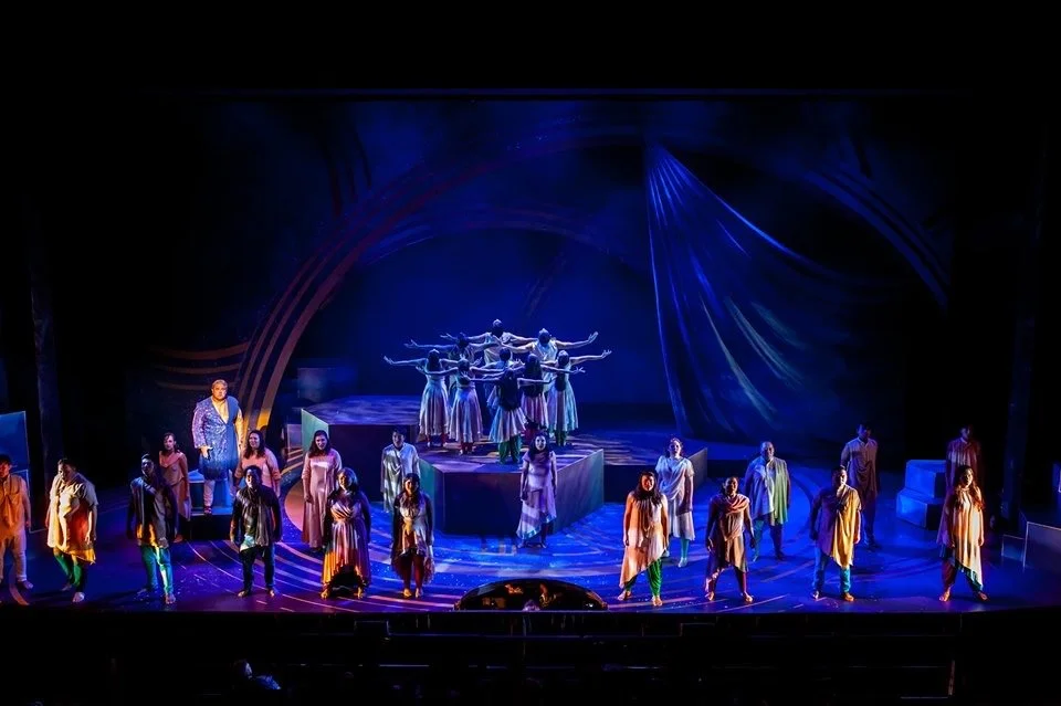 CHILDREN OF EDEN a Broadway musical by I'm A Bright Kid Foundation at Paliku Theatre. A stage performance featuring a group of performers, some on a raised platform, with dramatic lighting and colorful costumes.