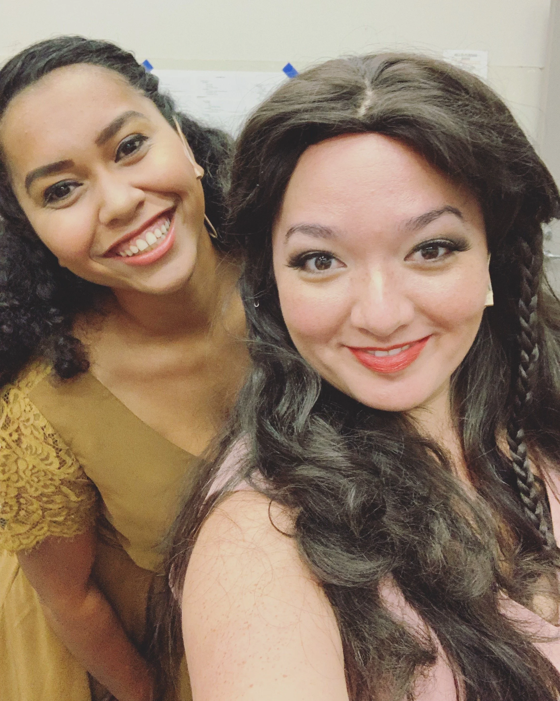 CHILDREN OF EDEN a Broadway musical by I'm A Bright Kid Foundation at Paliku Theatre. Two smiling women taking a selfie together in an indoor setting backstage in wigs and costume.