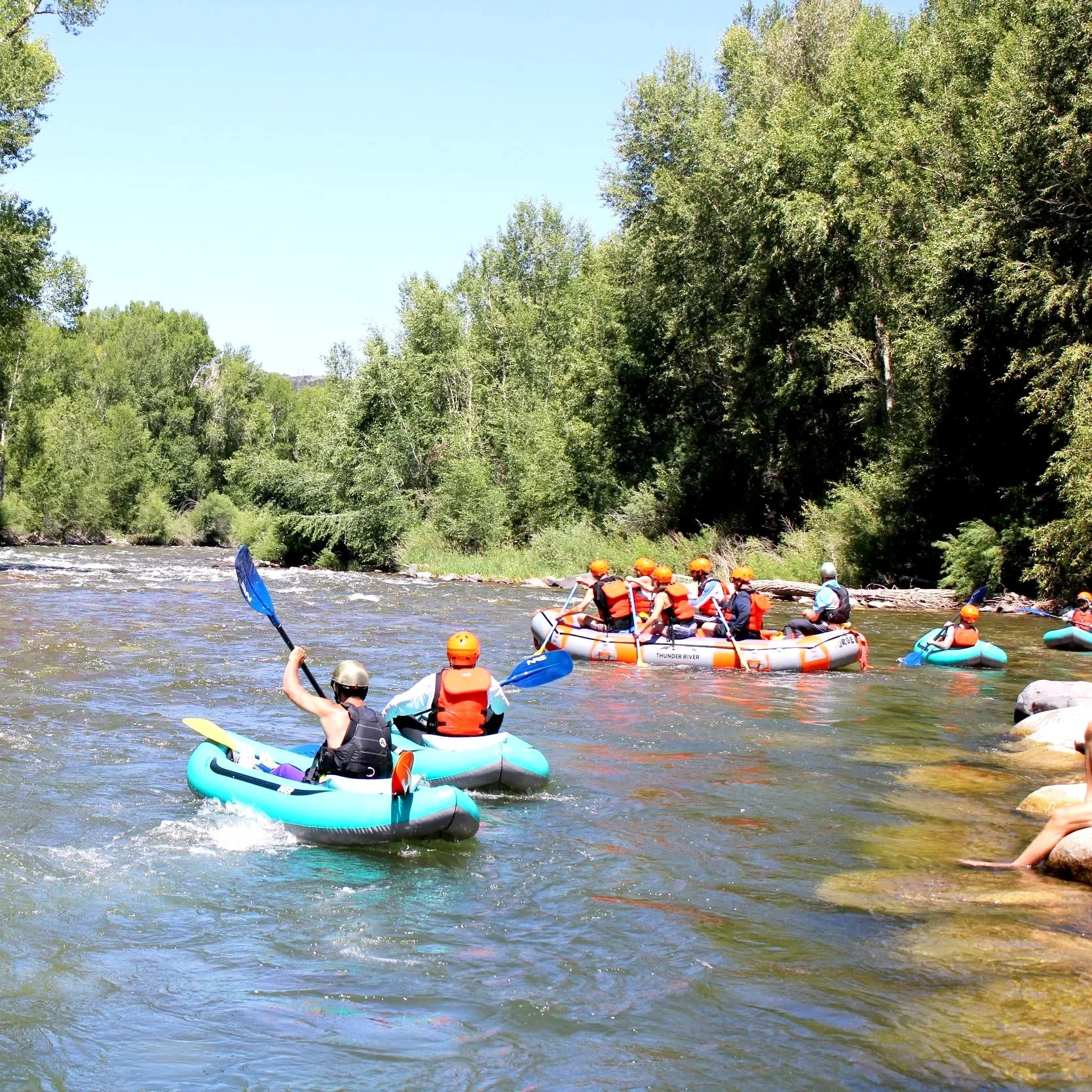 Group of people white water rafting on a river with green trees on the riverbank