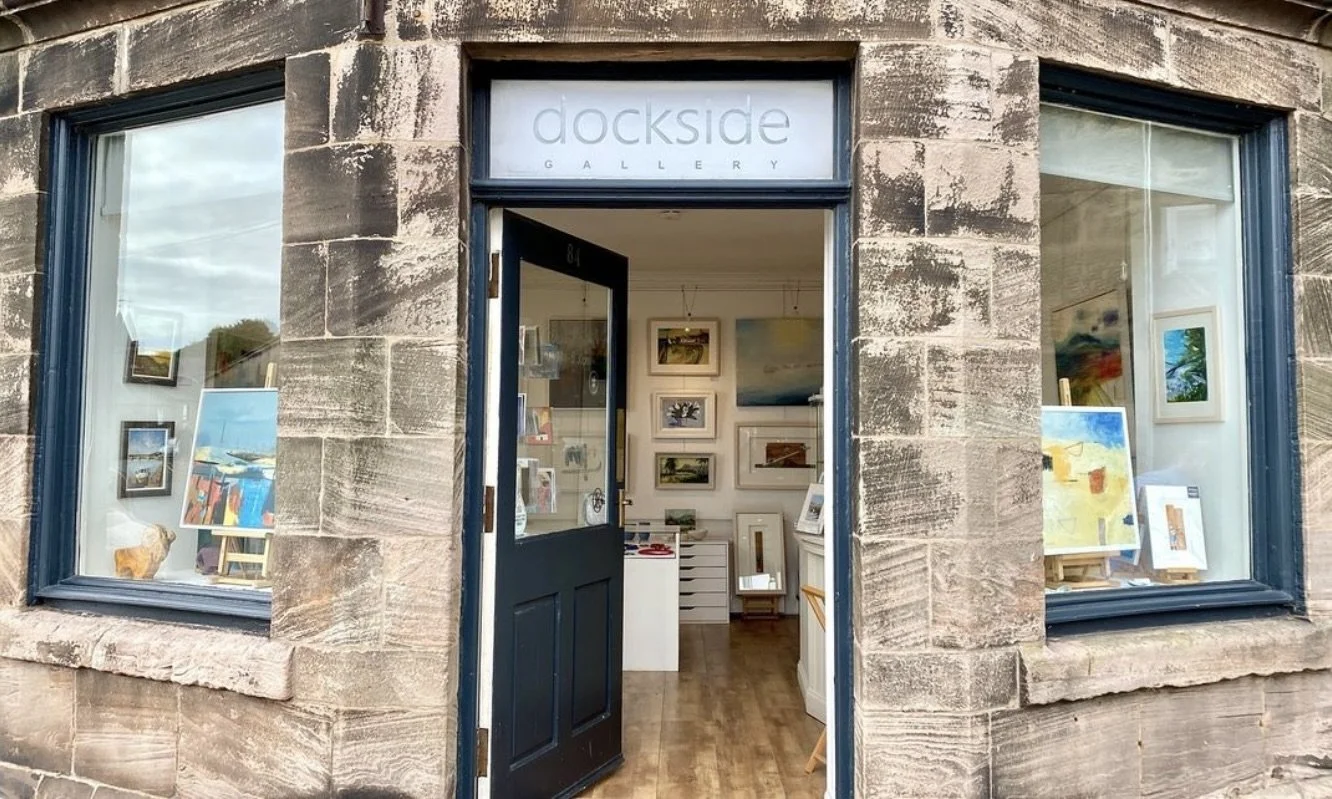 The entrance of Dockside Gallery, showing a dark door with a window, and large display windows on both sides with artworks inside.