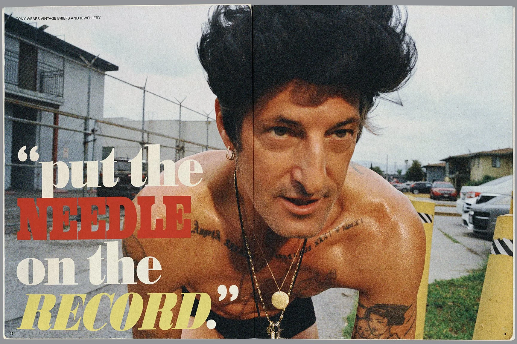 A man with black, styled hair, tattoos on his shoulders and chest, and wearing necklaces, looks into the camera with a serious expression. The background shows a parking lot with cars and a residential neighborhood. Overlay text says, "put the NEEDLE