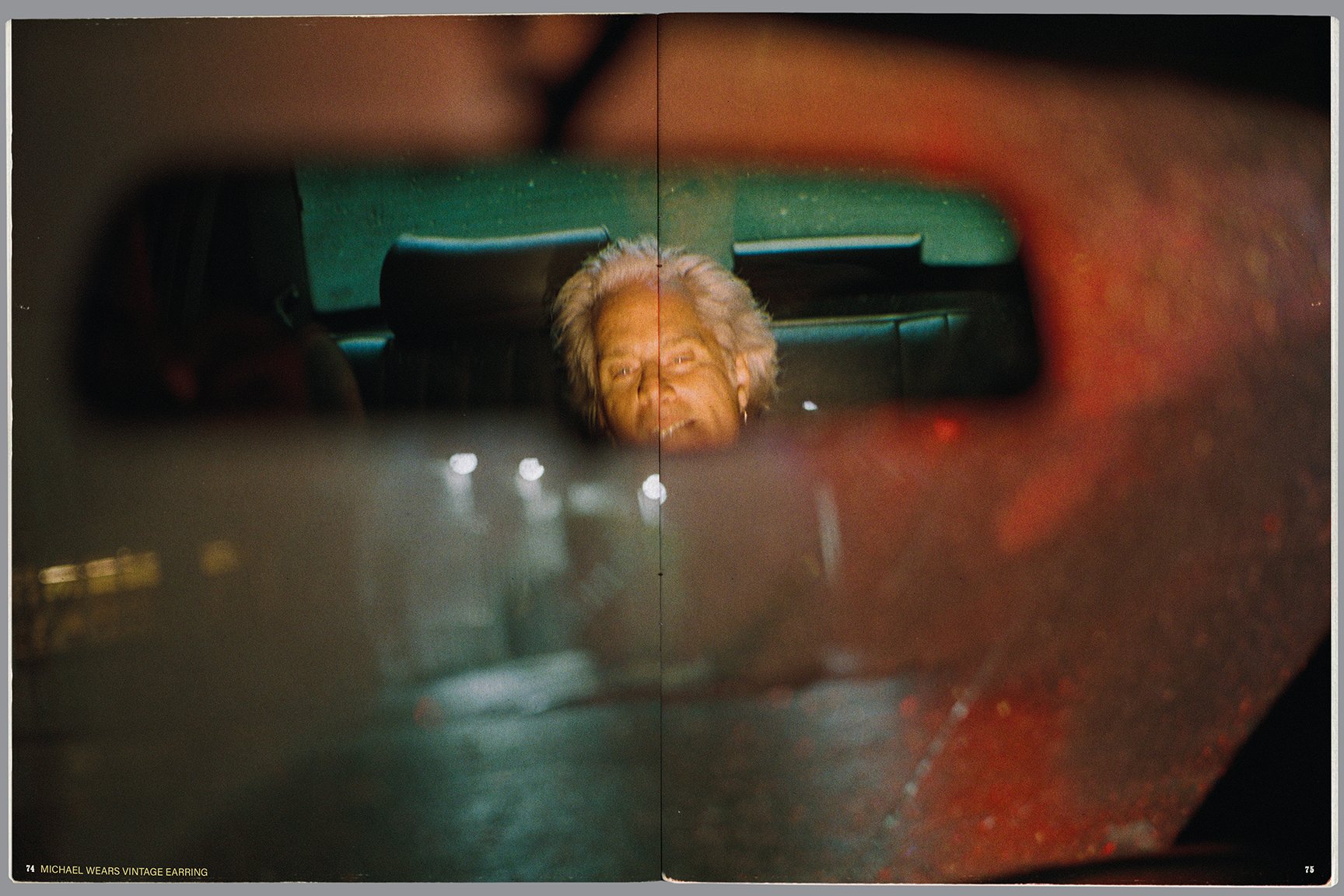 A woman with gray hair is looking into a rearview mirror of a car at night. The image captures her reflected face, with the car's interior and a dark background visible.