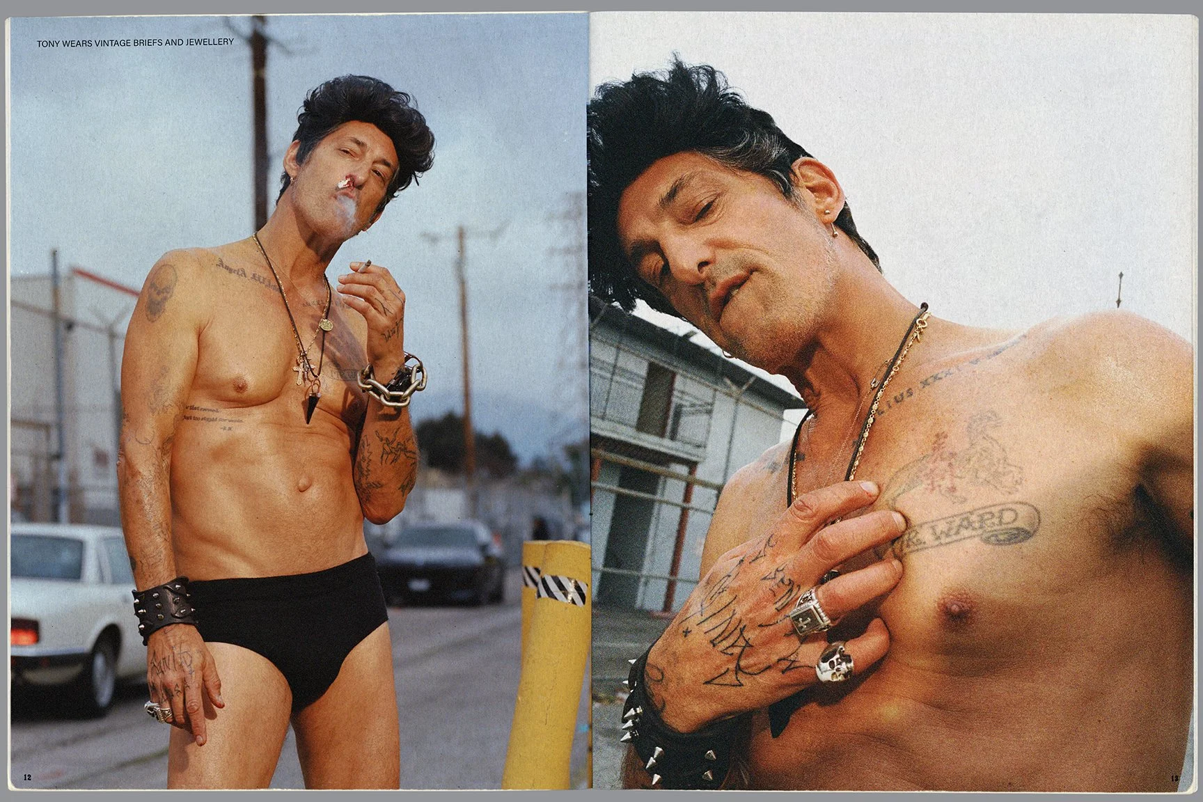 Two shirtless men with tattoos, jewelry, and punk style accessories. The man on the left stands outdoors in front of a street scene, wearing black briefs, with smoke on his upper lip, and looking at the camera. The man on the right is leaning against