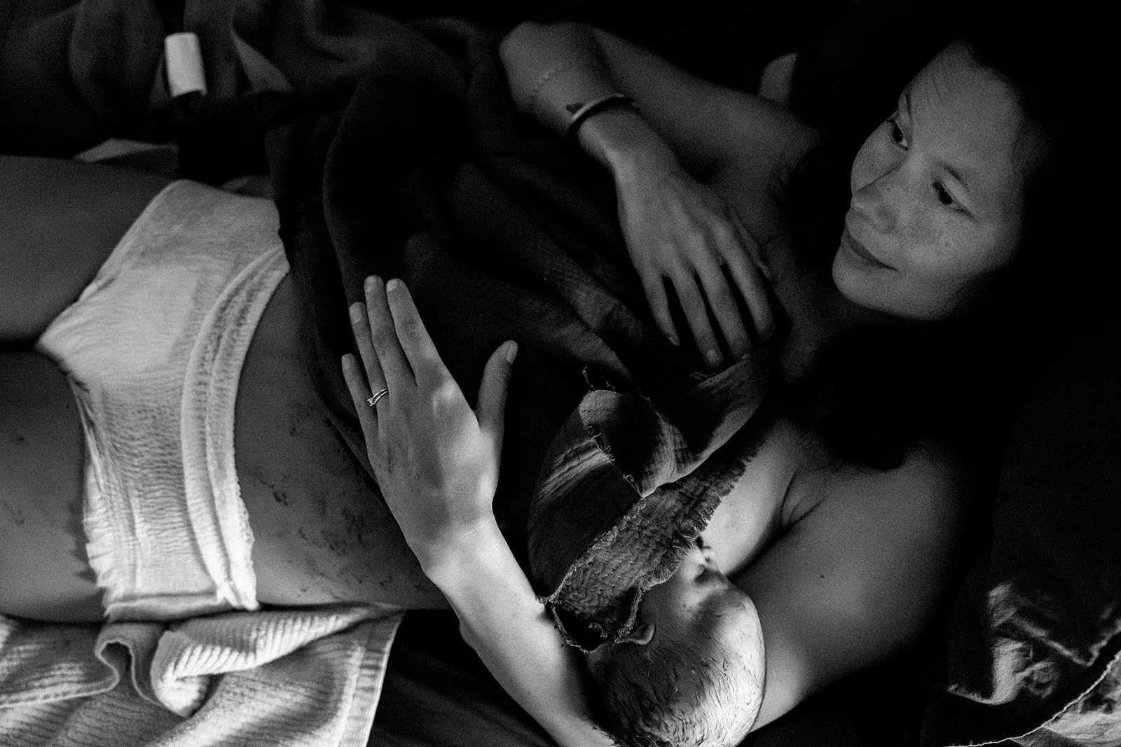A woman lying in bed holds a patient who has bandages on their head and arm, and appears to be resting or recovering.