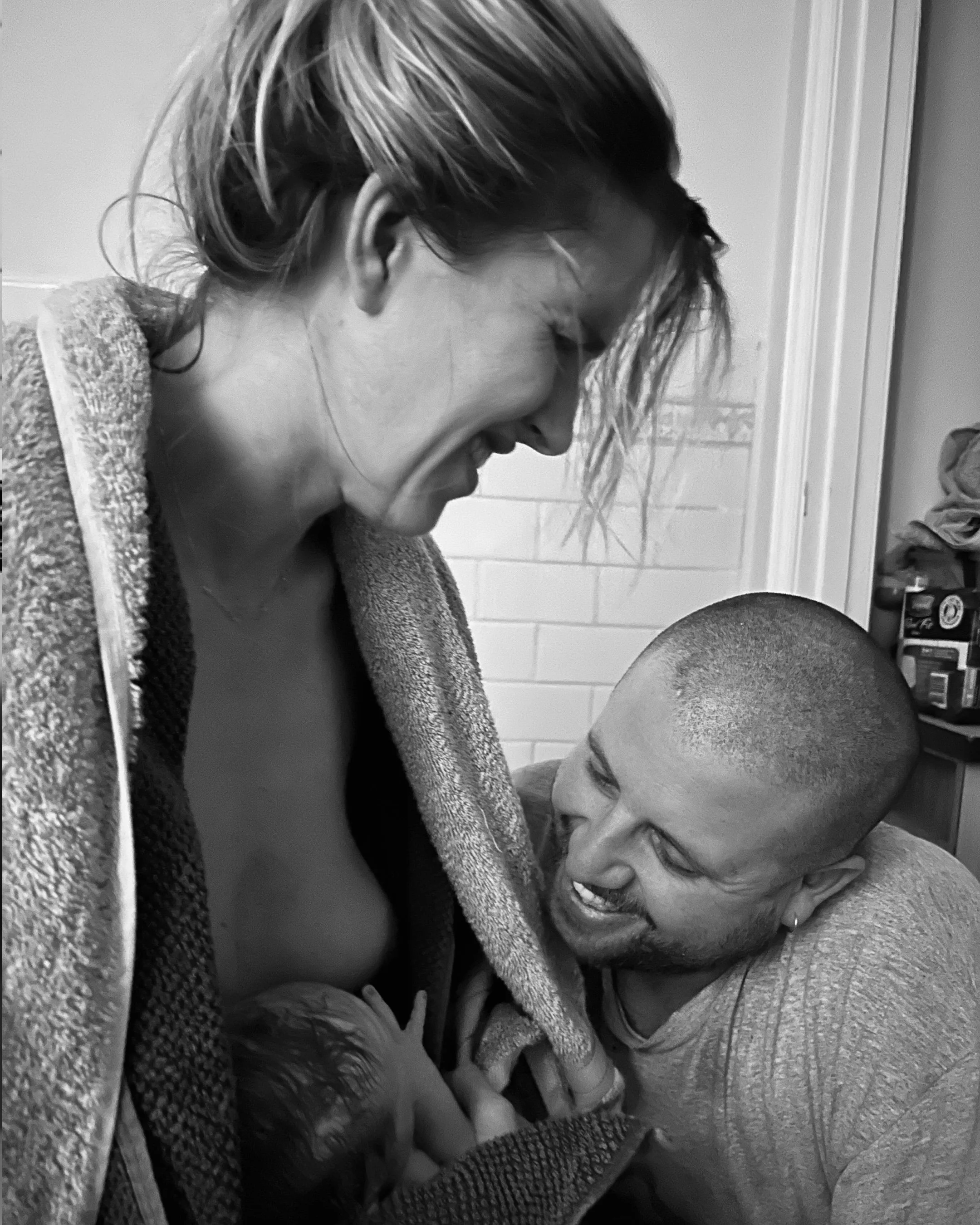 A woman and a young girl sharing a joyful moment, both smiling and leaning toward each other.