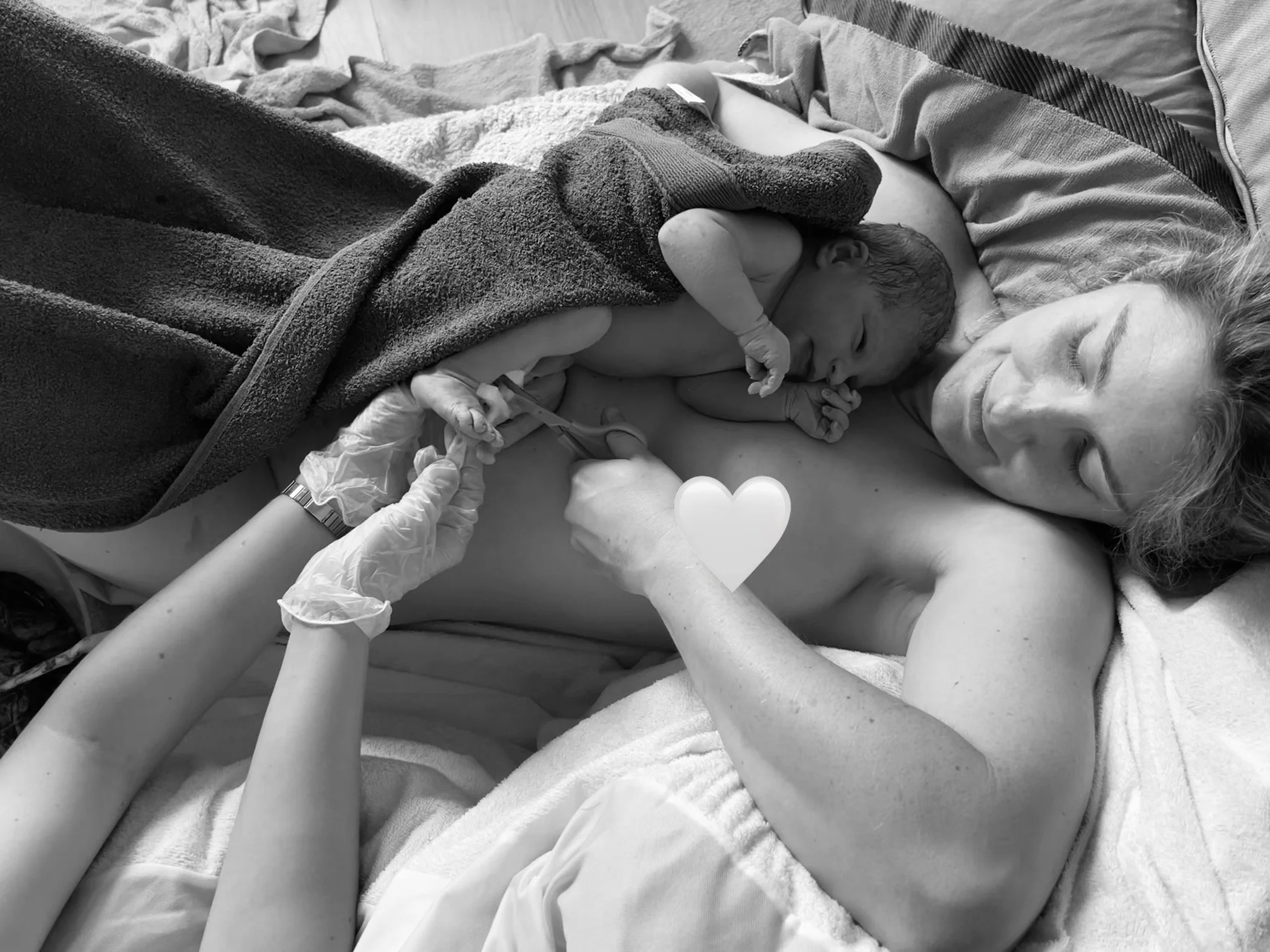 A newborn baby lying on a woman’s chest, with medical staff’s hands holding a syringe near the baby's arm, suggesting a medical procedure or injection.