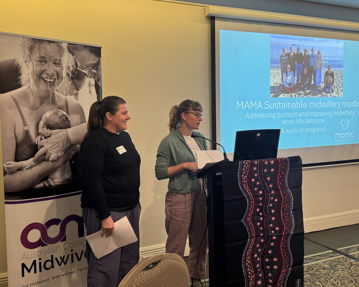 Two women presenting at a conference with a presentation slide titled "MAMA Sustainable midwifery model" and a group photo on the slide. A banner for the Australian College of Midwives is visible next to them.