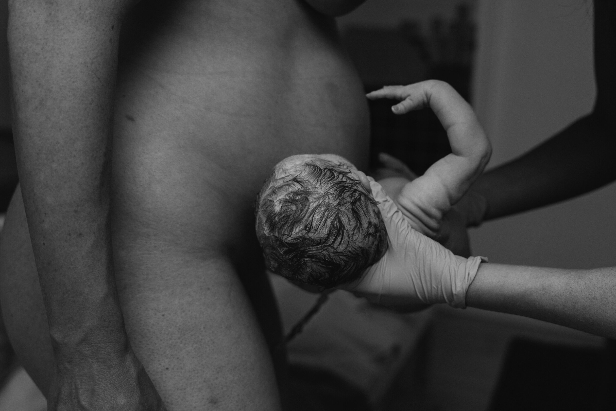 A newborn baby with wet hair being held by a person in a hospital setting.