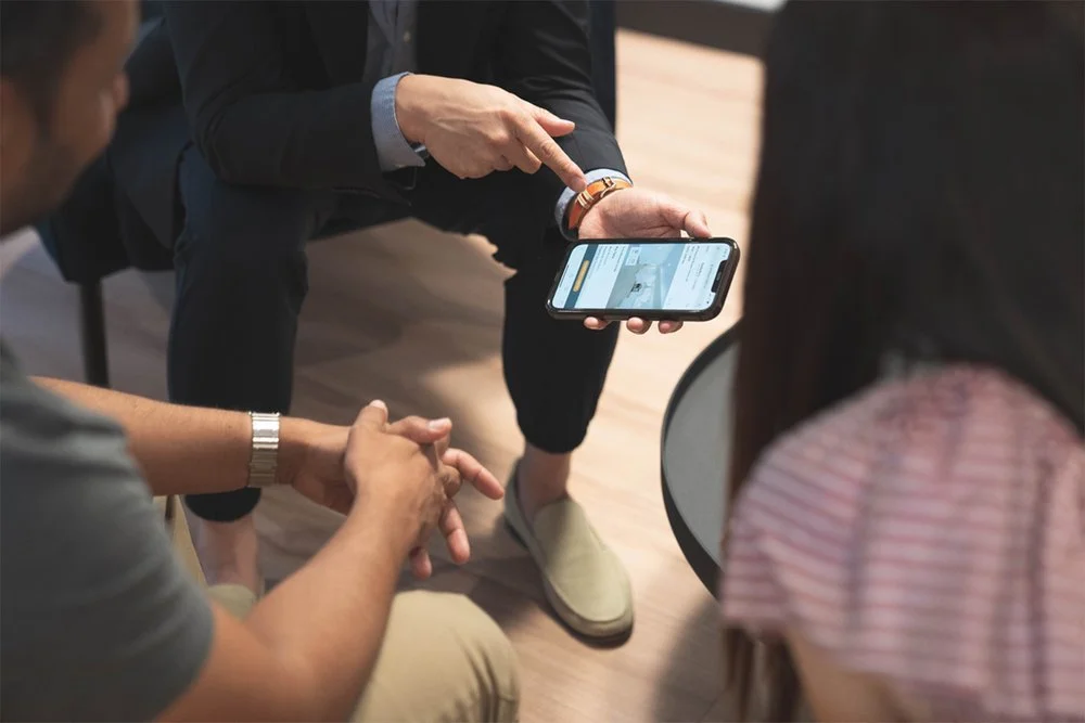 Three people sitting around a table, one person showing something on a smartphone to the others.