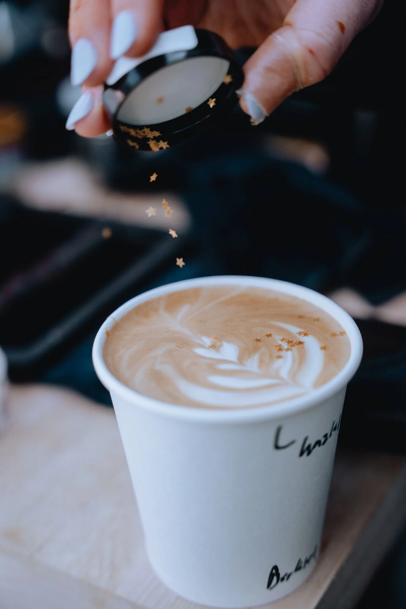 A cup of coffee with latte art on top, being poured from a container with gold star decorations.