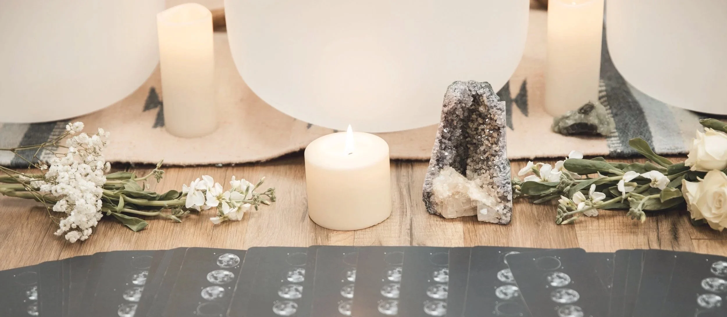 A wooden table decorated with white flowers, candles, and crystals, with tarot cards laid out in front.