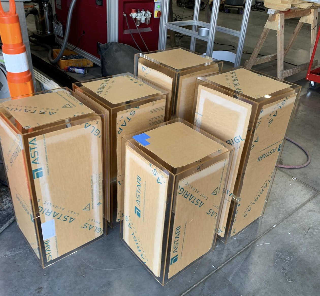 Several large glass enclosures with protective packaging labeled from Astari in a workshop or factory setting.