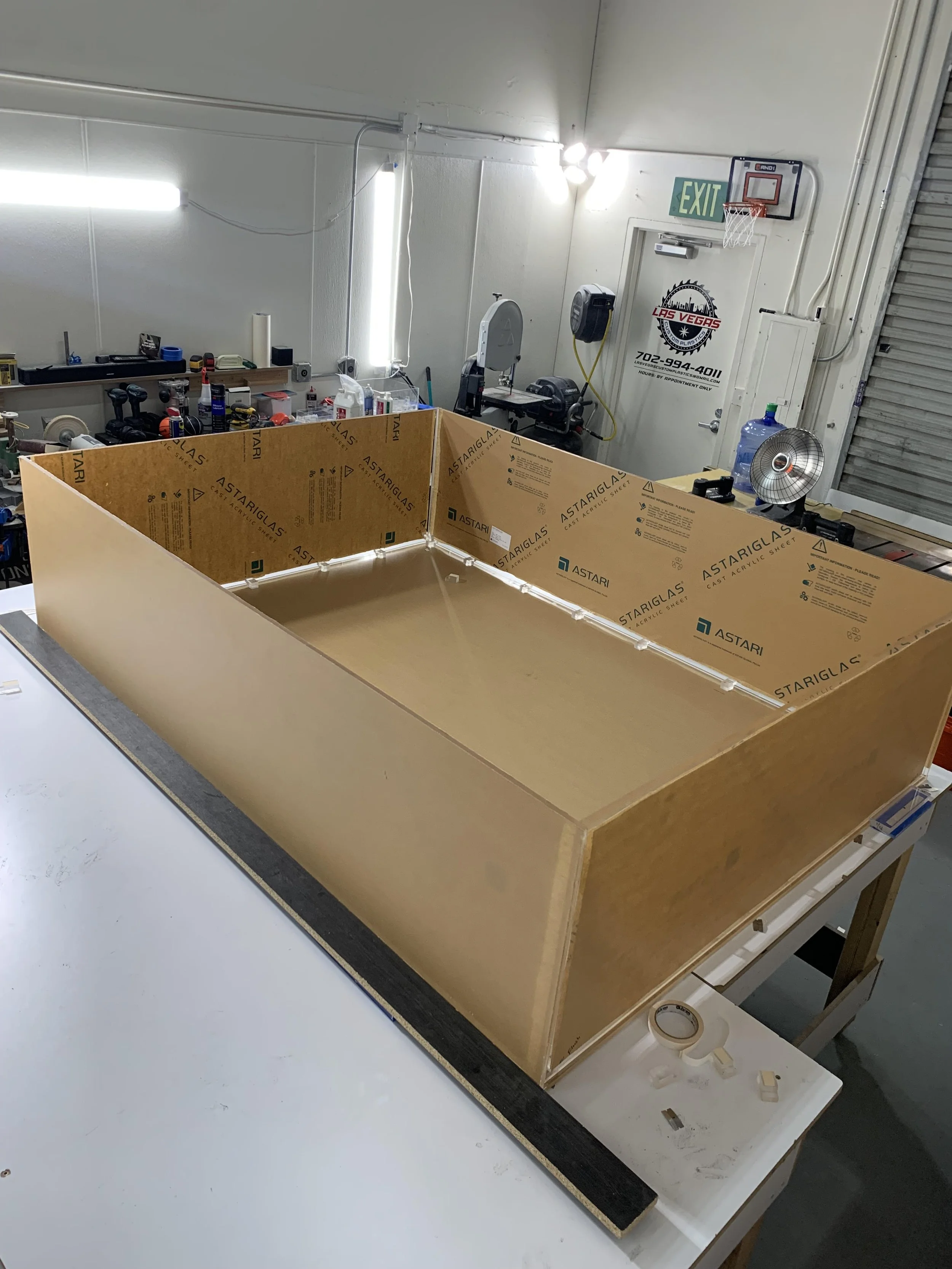 A workshop or craft area with a plywood framework, tools, supplies, and a basketball hoop with a backboard on a wall.