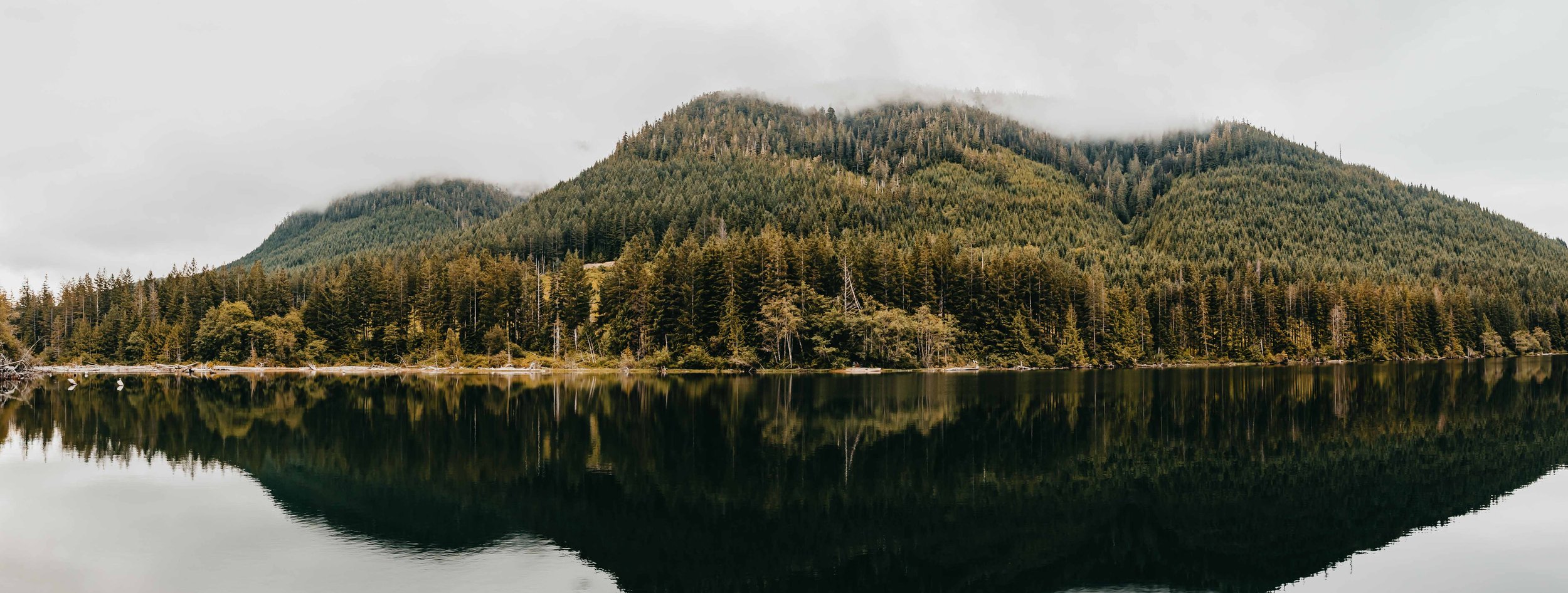 a panoramic photo of a remote backcountry lake with mountains reflecting the water on vancouver island british columbia