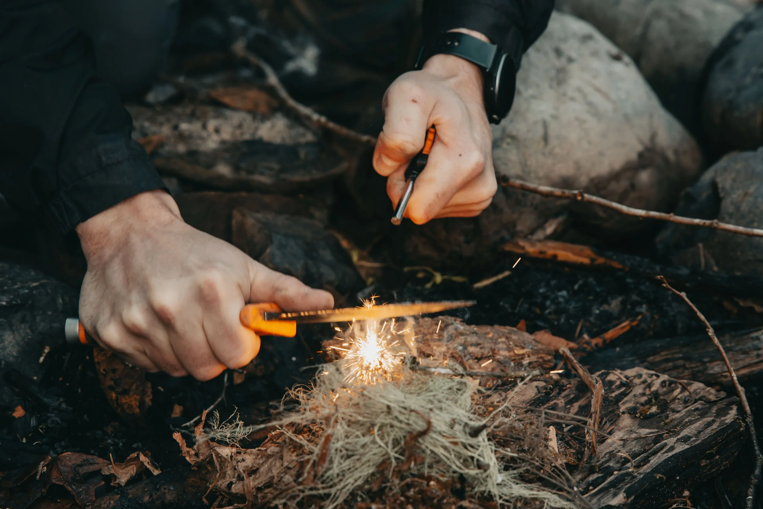 Person using a Light my Fire Ferrocerium Rod to start a campfire with sparks flying, outdoors on rocky ground.