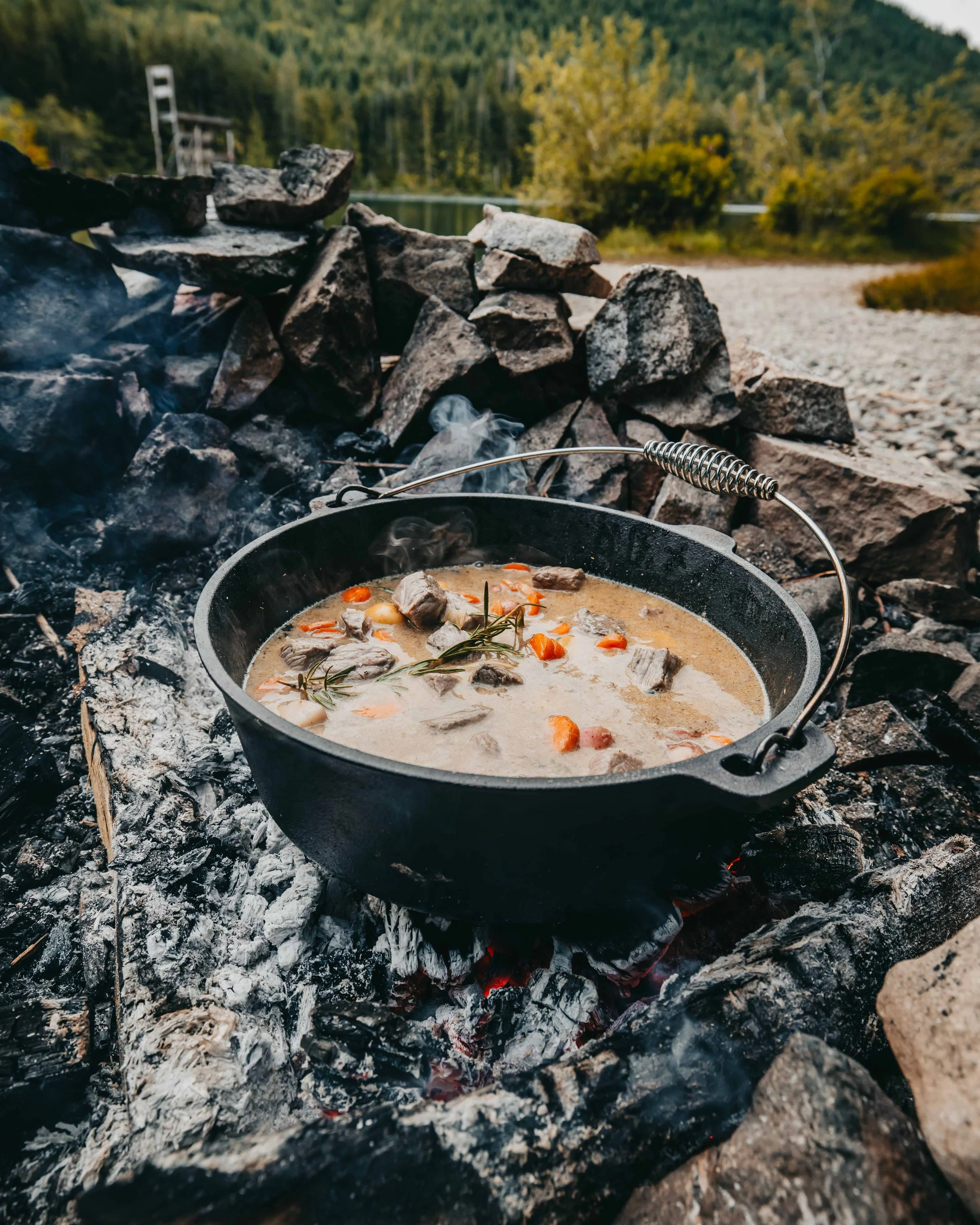 a cast iron pot of beef stew simmers and steams on the coals of a camp fire near a remote lake on vancouver island british columbia