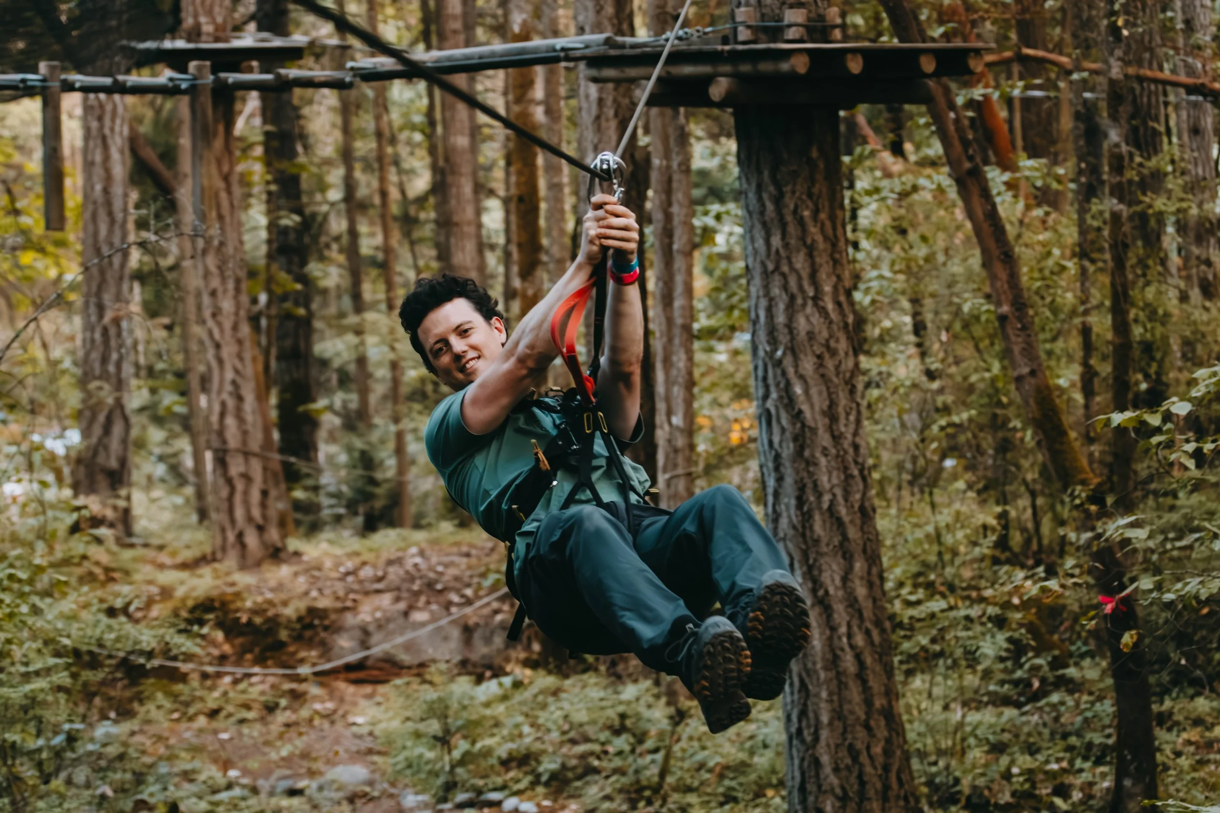 Person smiling and holding onto a zip line handle on a zip lining adventure on Vancouver Island