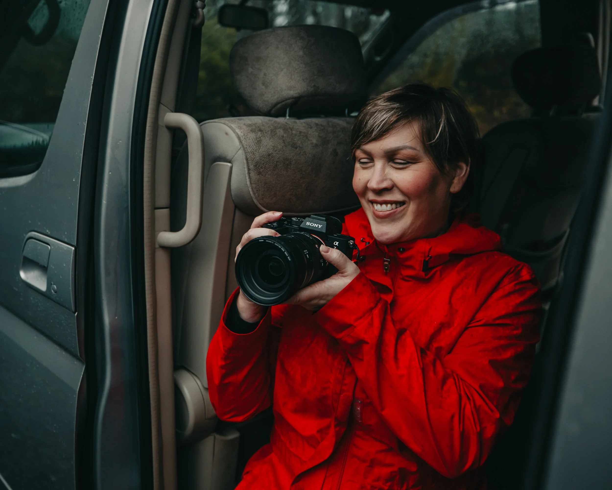 portrait of a woman in a bright red jacket reviewing images on her digital camera, Vancouver Island British Columbia