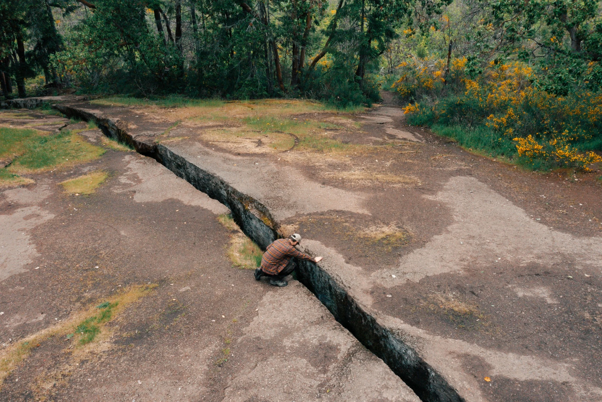 A hiker peering into The Abyss in Nanaimo, British Columbia, with rugged rock, forest, and dramatic depth highlighting the geological feature.