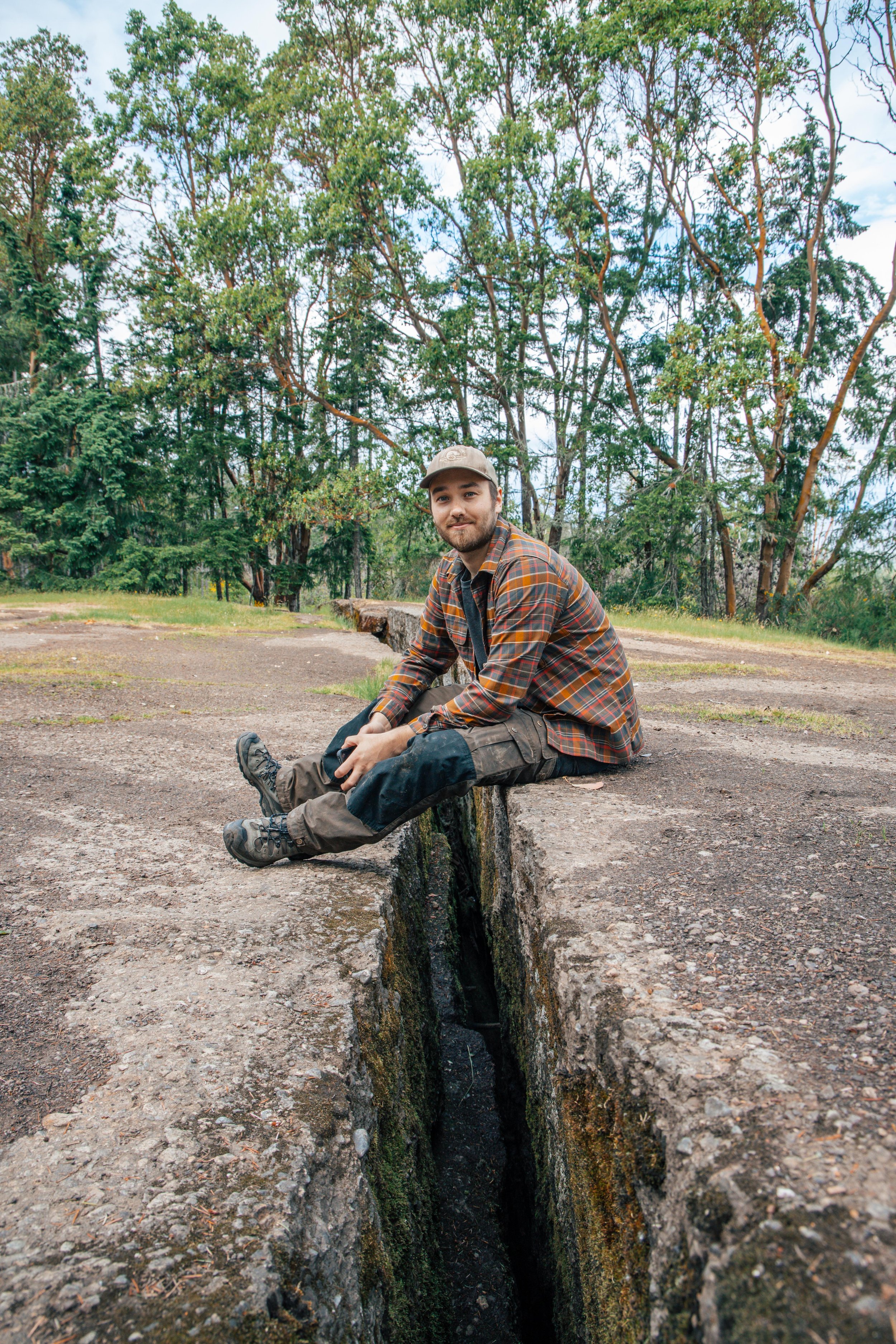 A hiker perched on the rocky edge above The Abyss in Nanaimo, BC, with the deep earth fissure and surrounding forest visible on Vancouver Island.