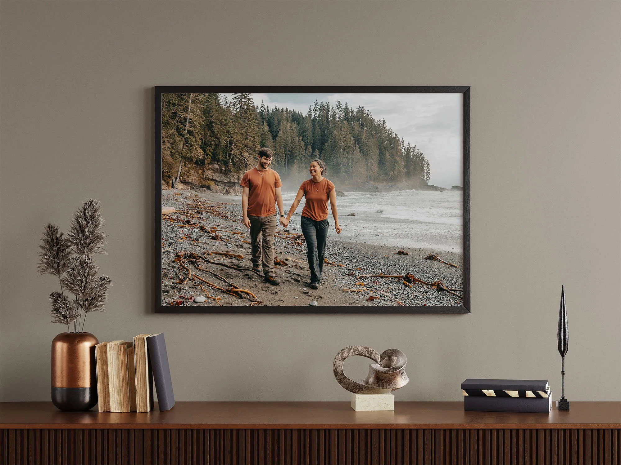A framed photo of a man and woman walking hand-in-hand along a beach with trees in the background at sombrio beach on vancouver island