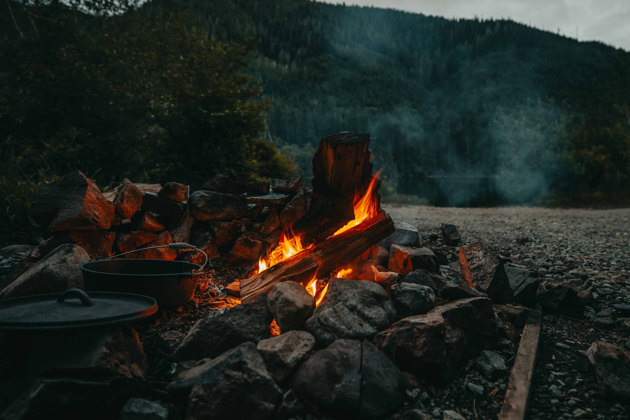 a campfire roars next to a backcountry lake at dusk on vancouver island british columbia